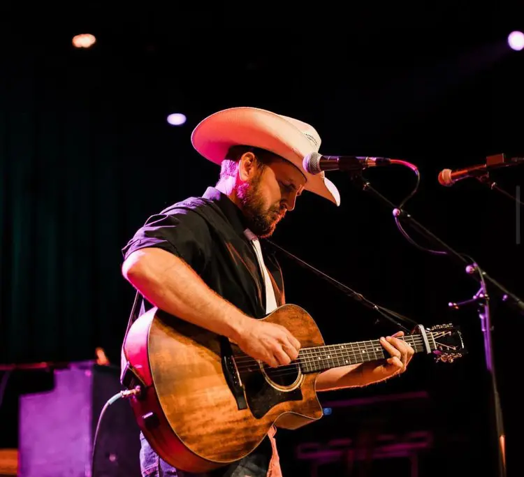 A man in cowboy hat playing guitar on stage.